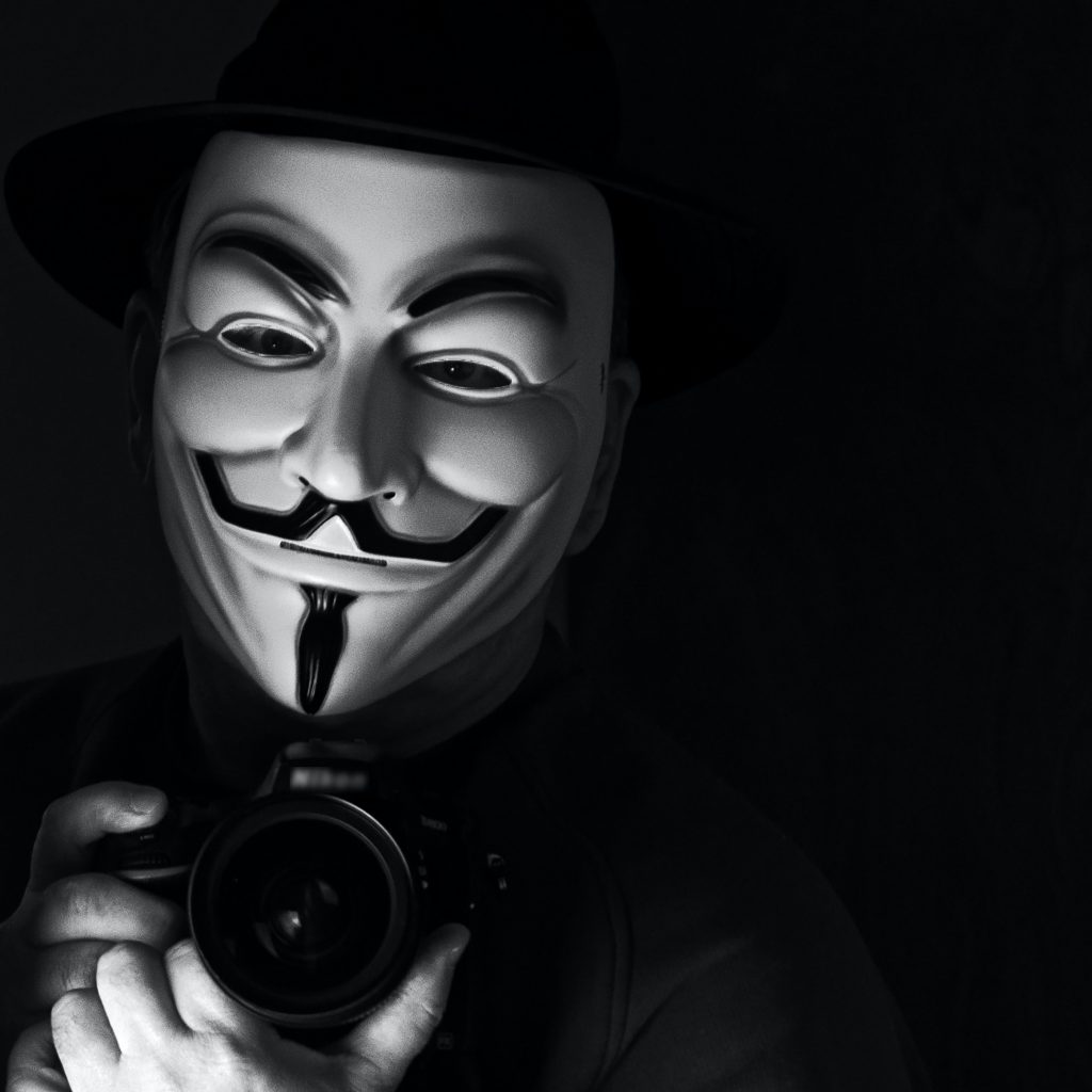 grayscale photography of person wearing guy fawkes mask while holding Nikon camera